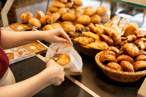 Verkäuferin verpackt frische Brötchen an der Bäckertheke